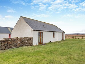 A single-story house with a sloped roof, a stone wall in front, and a grassy yard. - 2 bedroom accommodation in Mey, near Thurso (Mey, near Thurso)