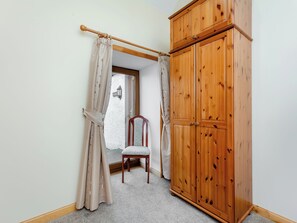 A room with a wooden wardrobe, a chair, and a window with curtains. - 2 bedroom accommodation in Mey, near Thurso (Mey, near Thurso)