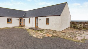 A two-story building with a stone foundation, a gravel driveway, and a stone wall. - 2 bedroom accommodation in Mey, near Thurso (Mey, near Thurso)