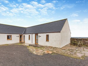 A two-story building with a stone foundation, a gravel driveway, and a stone wall. - 2 bedroom accommodation in Mey, near Thurso (Mey, near Thurso)