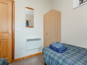 Ein Schlafzimmer mit Holztür, einem Spiegel, einem Kleiderschrank, einem Heizkörper und einem Bett mit kariertem Überwurf.