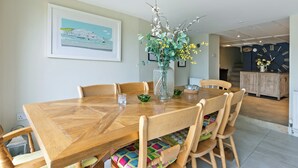 A dining area with a wooden table, chairs, a vase with flowers, a framed picture on the wall, and a clock. - 3 bedroom accommodation in 11 Above Town (11 Above Town)