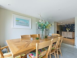 Uma sala de jantar com mesa de madeira, cadeiras, um vaso com flores, um quadro na parede e um relógio.