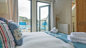A bedroom with a bed, a view of the sea, a balcony with chairs, and a wooden door. - 3 bedroom accommodation in 11 Above Town (11 Above Town)