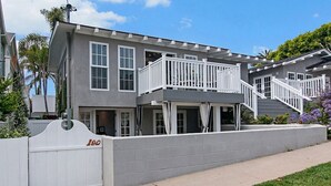 Une maison à deux étages, avec une façade grise, des balustrades blanches et un portail blanc portant le numéro « 180 ».