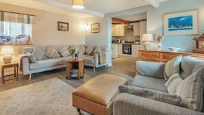 A living room with a sofa, ottoman, and a coffee table with a bottle and glasses. - 3 bedroom accommodation in Llanfwrog, near Holyhead (Llanfwrog, near Holyhead)