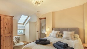 A bedroom with a large bed, a wooden wardrobe, a small armchair, and a skylight. - 3 bedroom accommodation in Llanfwrog, near Holyhead (Llanfwrog, near Holyhead)