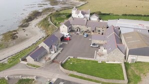 A coastal building with a parking area, a grassy field, and a view of the sea. - 3 bedroom accommodation in Llanfwrog, near Holyhead (Llanfwrog, near Holyhead)