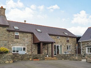 A stone building with a sloped roof, multiple windows, and a small porch area. - 3 bedroom accommodation in Llanfwrog, near Holyhead (Llanfwrog, near Holyhead)