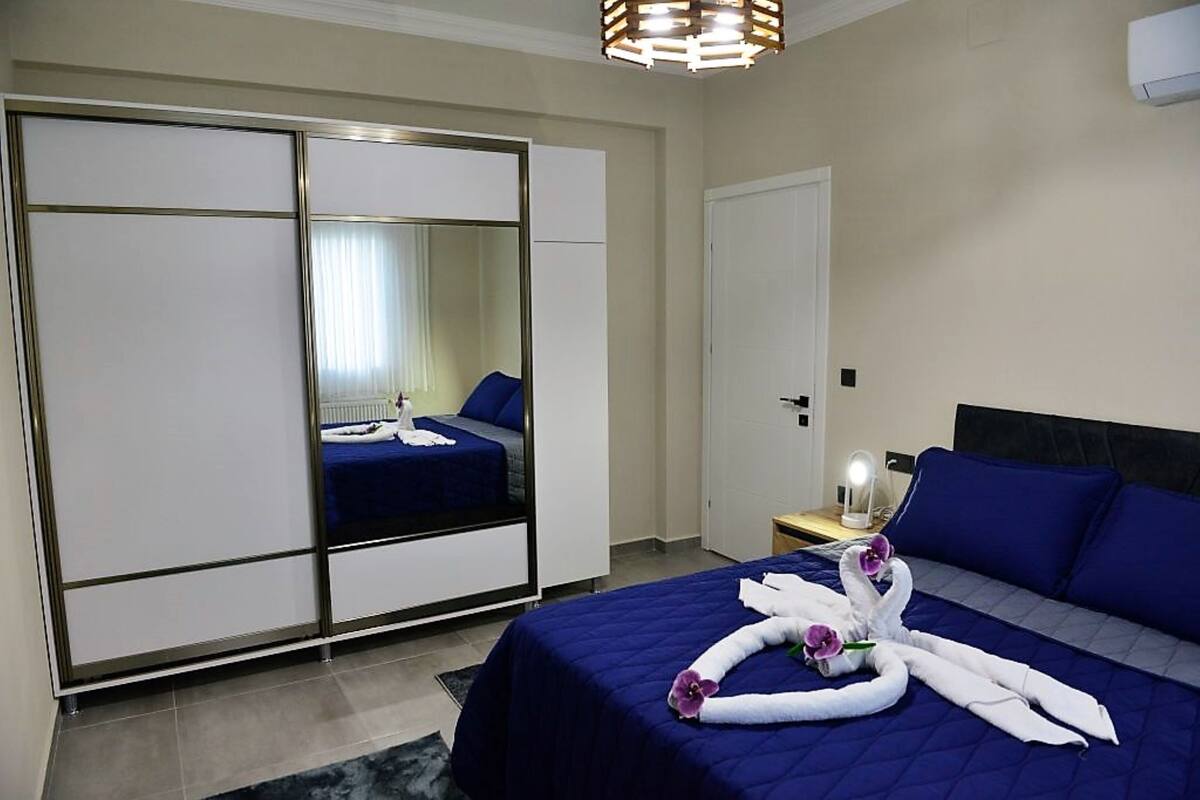 A hotel room with a bed, a wardrobe, a mirror, and a nightstand with a lamp.