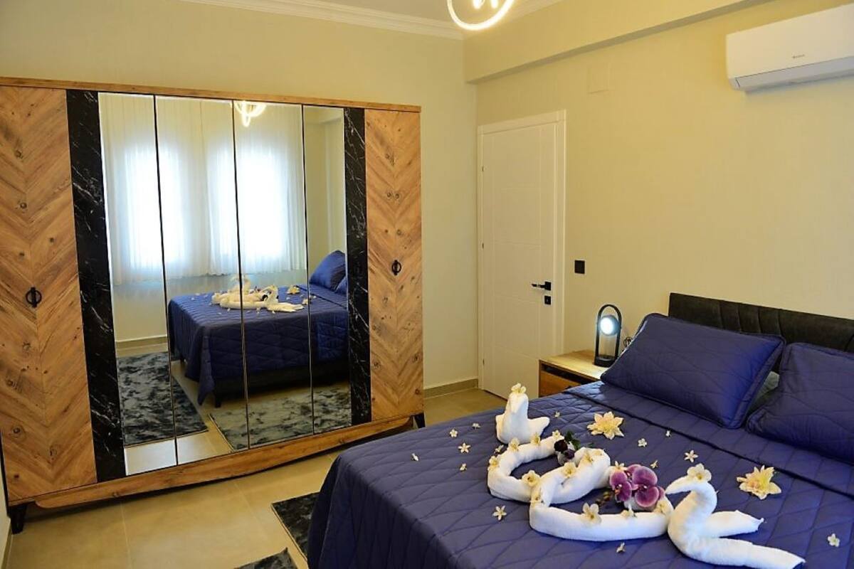 A bedroom with a large mirror, a bed with blue bedding, and a decorative arrangement of towels and flowers on the bed.