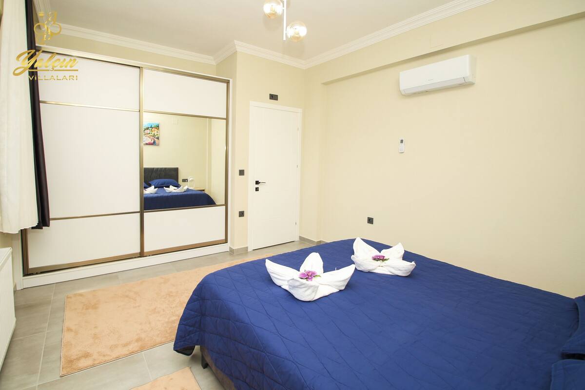 A hotel room with a large mirror, a bed with blue bedding, and a white air conditioning unit on the wall.