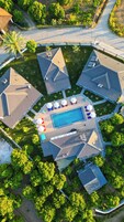 Vista aérea de un complejo turístico con una piscina central, varias áreas cubiertas y abundante vegetación.