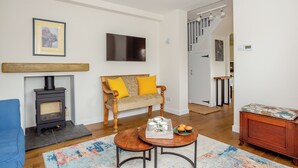 Una sala de estar con chimenea, sofá, mesa de centro y una escalera que lleva a otra habitación.