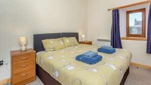 Ein Schlafzimmer mit einem Bett, zwei Nachttischen, einem Fenster mit Vorhängen und einem Heizkörper.