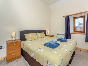 A bedroom with a bed, two bedside tables, a window with curtains, and a radiator.