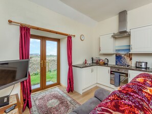 Une cuisine moderne avec des armoires blanches, une hotte de cuisinière en acier inoxydable et une vue sur la campagne, visible à travers une porte-fenêtre coulissante.