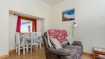 A living room with a brown sofa, a dining table with chairs, a red curtain, and a painting of a beach scene.
