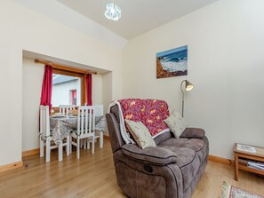Un salon avec un canapé marron, une table à manger avec des chaises, un rideau rouge et un tableau représentant une scène de plage.