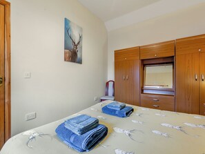 Une chambre à coucher avec un lit, une armoire en bois, un tableau représentant un cerf et une chaise.