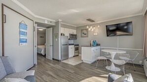 A modern living room with a sofa, a dining area with a table and chairs, a kitchen with white cabinets and appliances, and a flat-screen TV mounted on the wall. - Beautiful Ocean Views, on 15th floor! (Myrtle Beach)