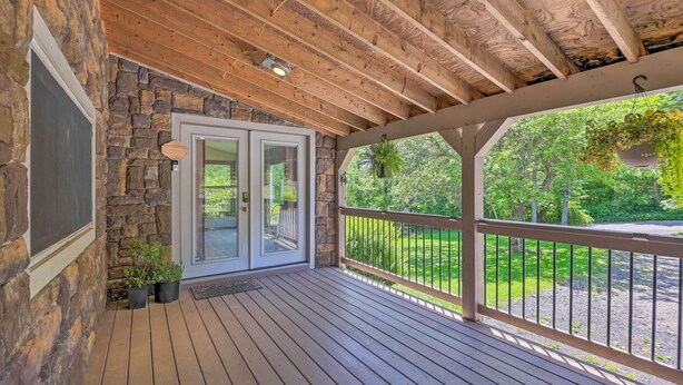 A covered porch with wooden beams, stone walls, and a view of a green landscape. - Relax & Renew in Serene Mountain Cottage (Albrightsville)