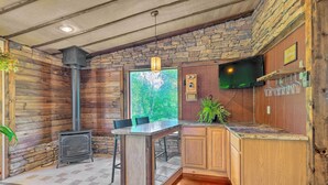 A rustic kitchen with a stone wall, wooden cabinets, a built-in bar, and a wood-burning stove. - Relax & Renew in Serene Mountain Cottage (Albrightsville)