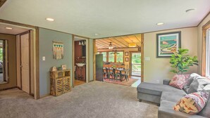 A spacious living room with a grey sofa, a dining area with a table and chairs, and a kitchen visible through an open doorway. - Relax & Renew in Serene Mountain Cottage (Albrightsville)