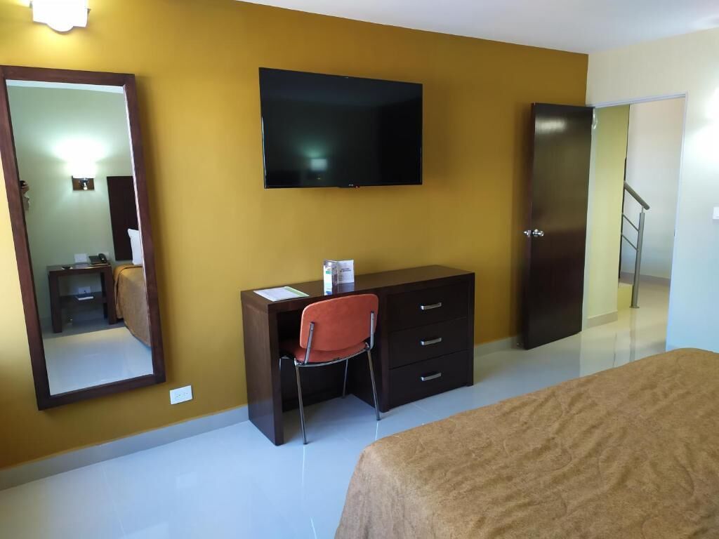 A hotel room with a bed, a desk with a chair, a television, a wardrobe, and a mirror.