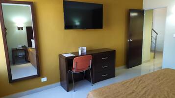 A hotel room with a bed, a desk with a chair, a television, a wardrobe, and a mirror.