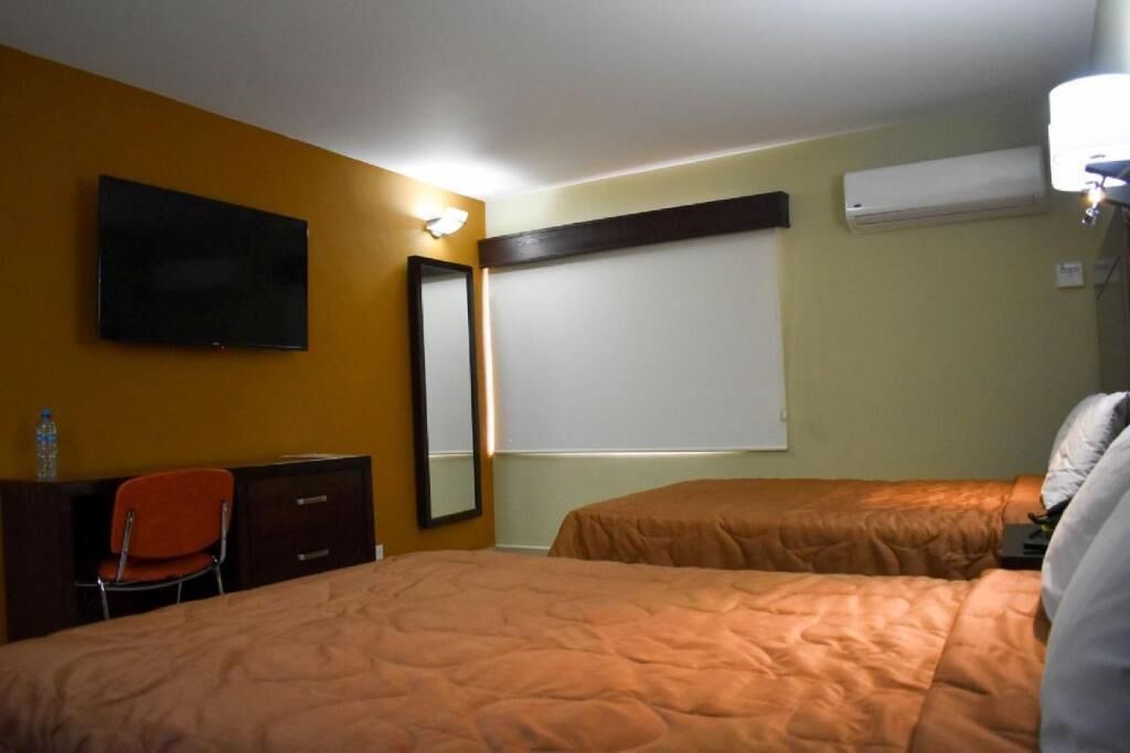 A hotel room with two beds, a TV, a desk, and an air conditioning unit.