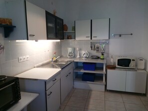 Una cocina compacta con armarios blancos, un lavamanos, una cafetera, un hervidor, un microondas y un tostador.