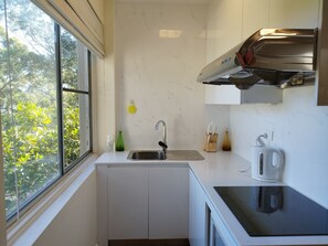 Enjoy a serene atmosphere with a view of lush greenery from the large window, while cooking in the kitchen with a sink and ample counter space.
