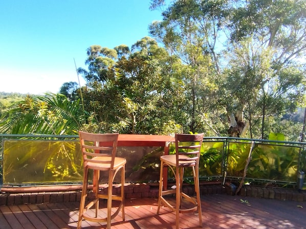 Relax in a serene outdoor space with a comfortable seating area featuring a table and two chairs on a spacious deck surrounded by lush greenery.