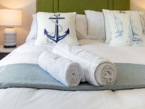 A neatly made bed with a rolled white towel, a pillow with an anchor design, and a pillow with sailboat illustrations.