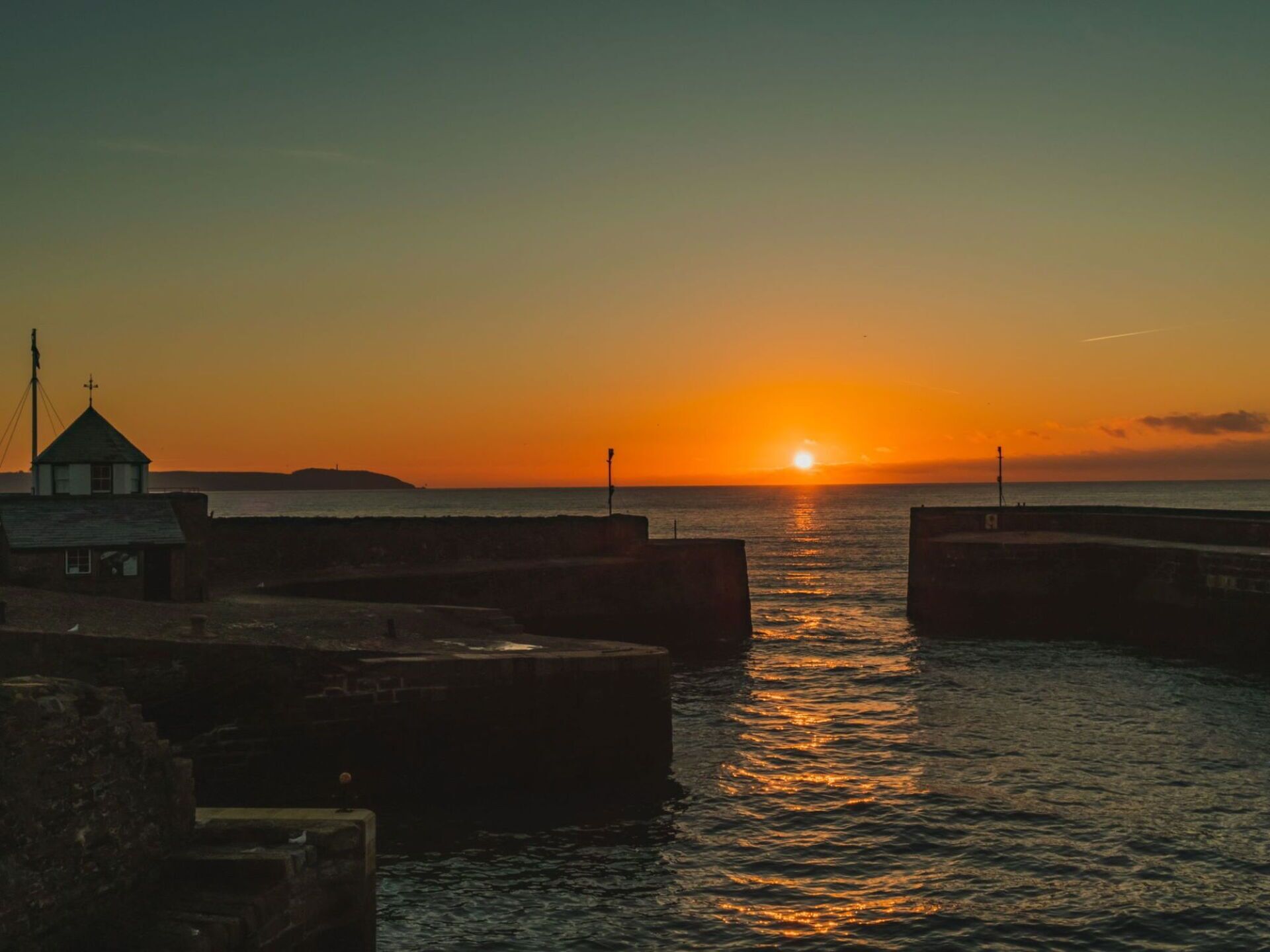 Un atardecer sobre un mar tranquilo con un muelle y un edificio pequeño a la izquierda.