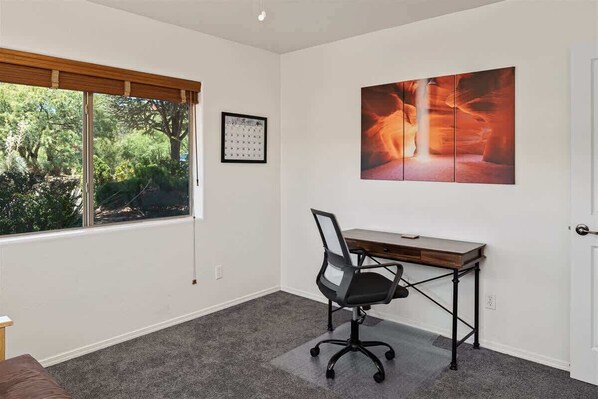 A room with a desk, chair, window, and artwork.