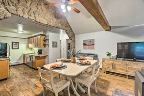 A dining area with a stone arch, wooden ceiling beams, a TV, and a kitchen in the background.