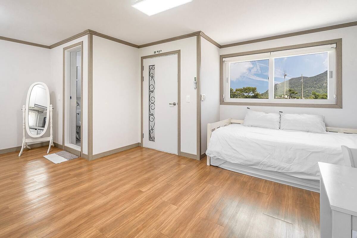 A bedroom with a bed, a window with a view, a door, and a mirror.