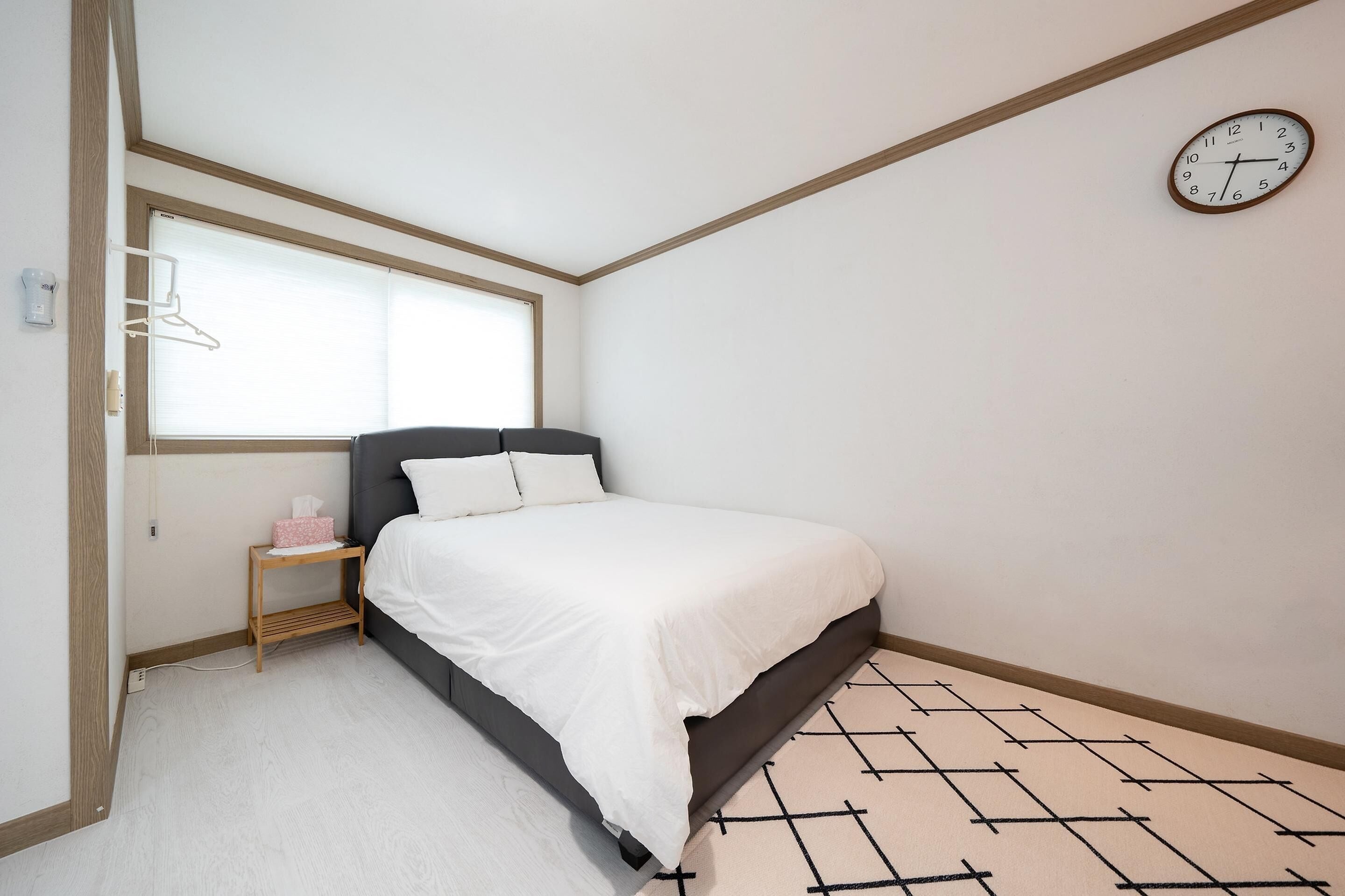 Una camera da letto con un letto, un comodino, una sveglia al muro e una finestra con persiane.
