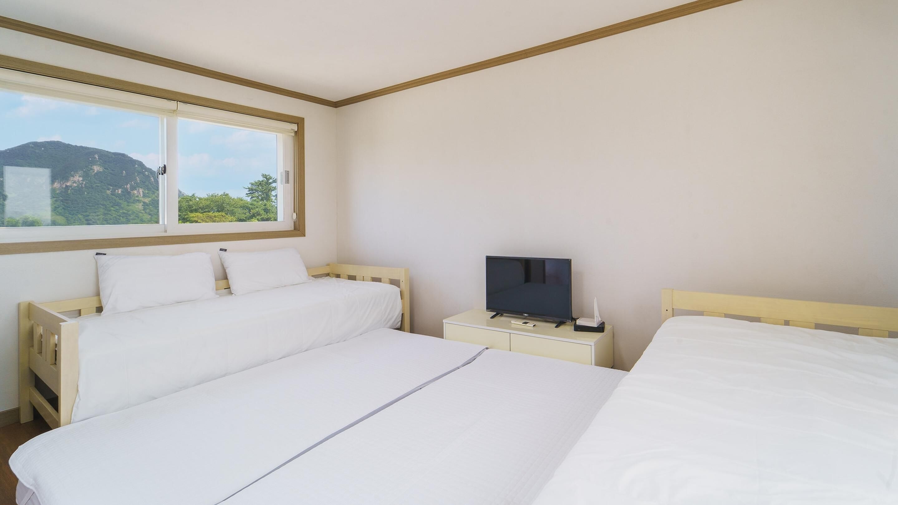 Ein Hotelzimmer mit zwei Einzelbetten, einem Fernseher auf einem Nachttisch und einem Fenster mit Blick auf die Berge.