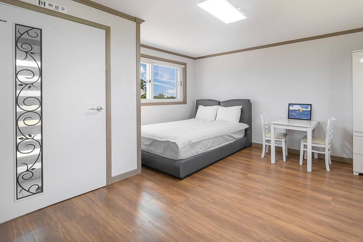 A bedroom with a bed, a desk, two chairs, a wardrobe, and a window.