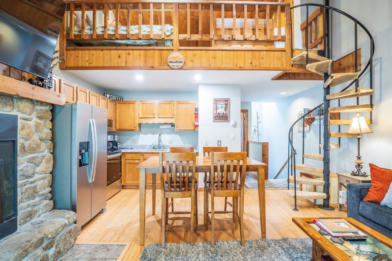 Un interior acogedor con cocina, comedor y un dormitorio en un altillo con escalera espiral.