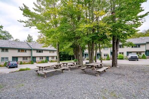 A campground with picnic tables, a gravel ground, and a row of buildings with a green roof.