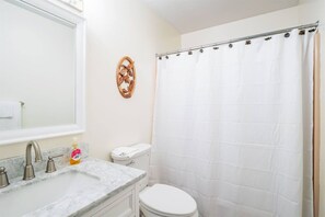 A bathroom with a white toilet, a sink with a marble countertop, and a shower curtain.