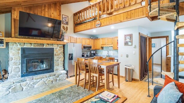 A cozy interior with a stone fireplace, wooden dining area, and a staircase leading to an upper level. - Northwoods F3 - Chill`inn Slopeside (Davis)