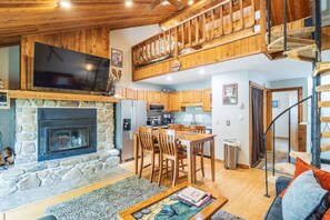 A cozy interior with a stone fireplace, wooden dining area, and a staircase leading to an upper level.