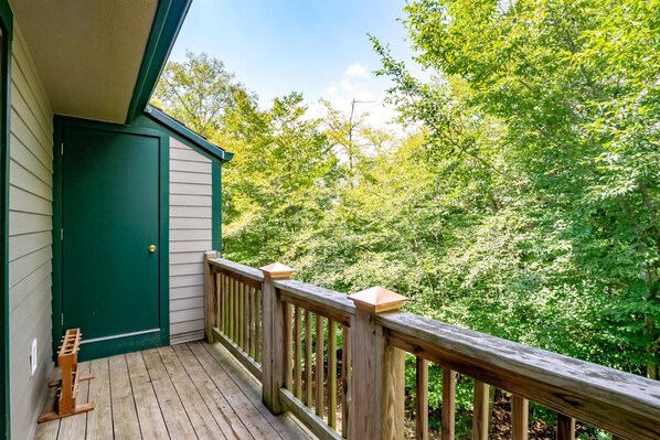 A wooden deck with a green door and a view of dense green foliage.