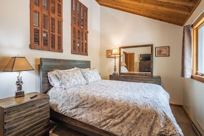 A bedroom with a wooden headboard, a bed with floral bedding, a nightstand with a lamp, and a mirror reflecting the room.