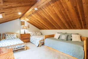 A cozy attic bedroom with two wooden beds, a dresser, and a small table.